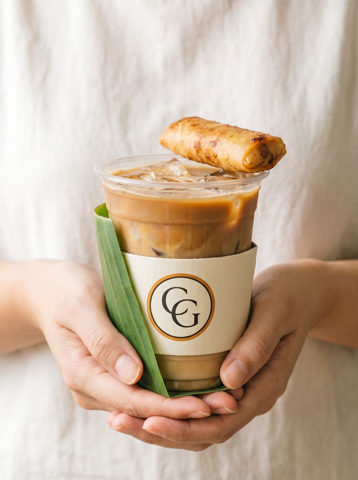 A pair of hands holding a Common Grounds Turon Latte with a banana leaf wrap