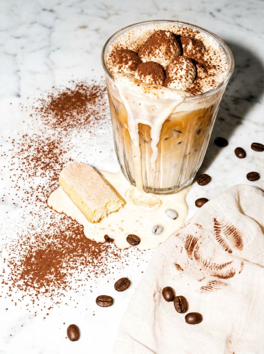 Tiramisu Dream iced latte dusted with cocoa, ladyfinger biscuit beside the glass